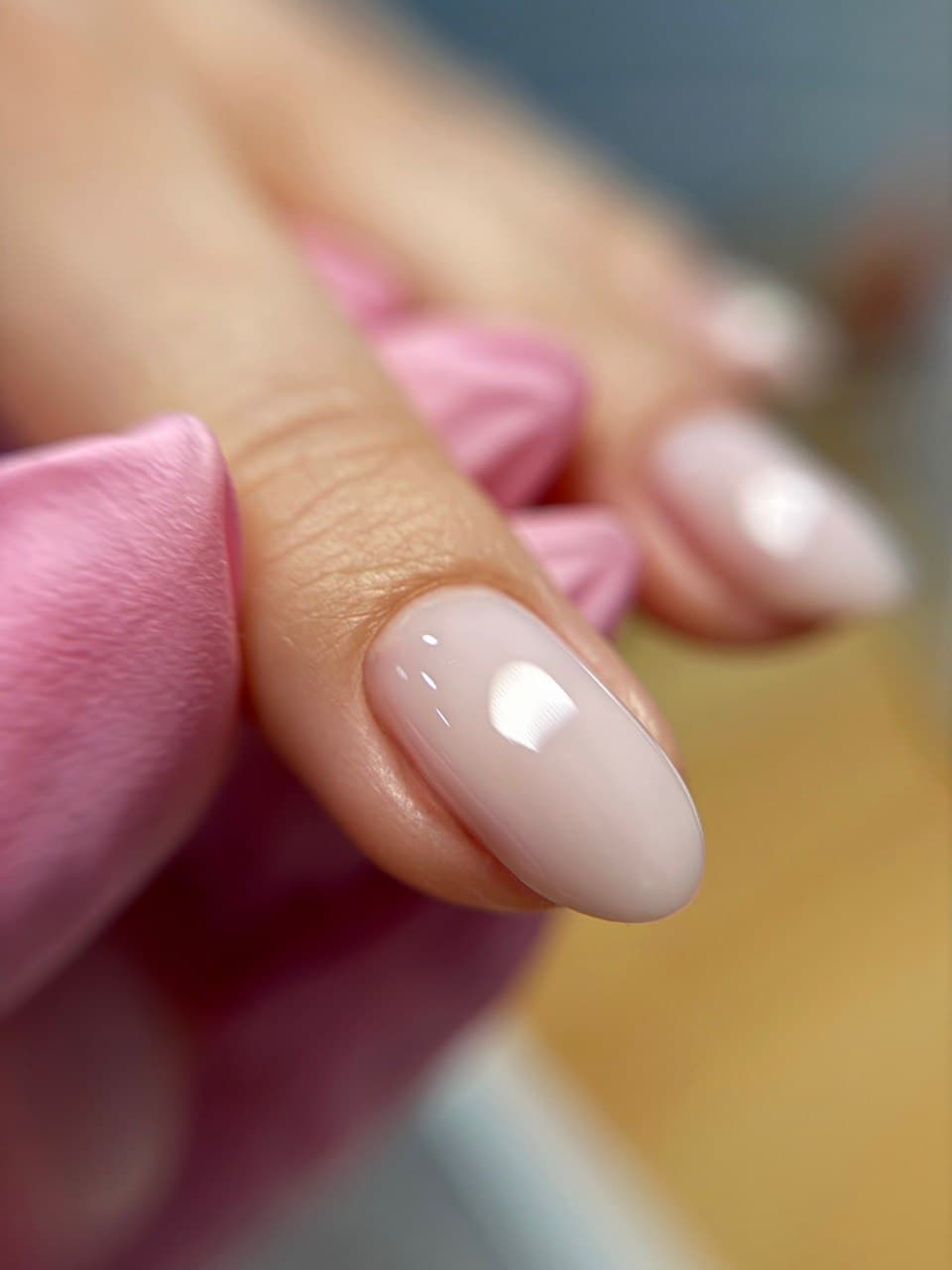 Nude almond nail — glossy natural finish with soft pink background